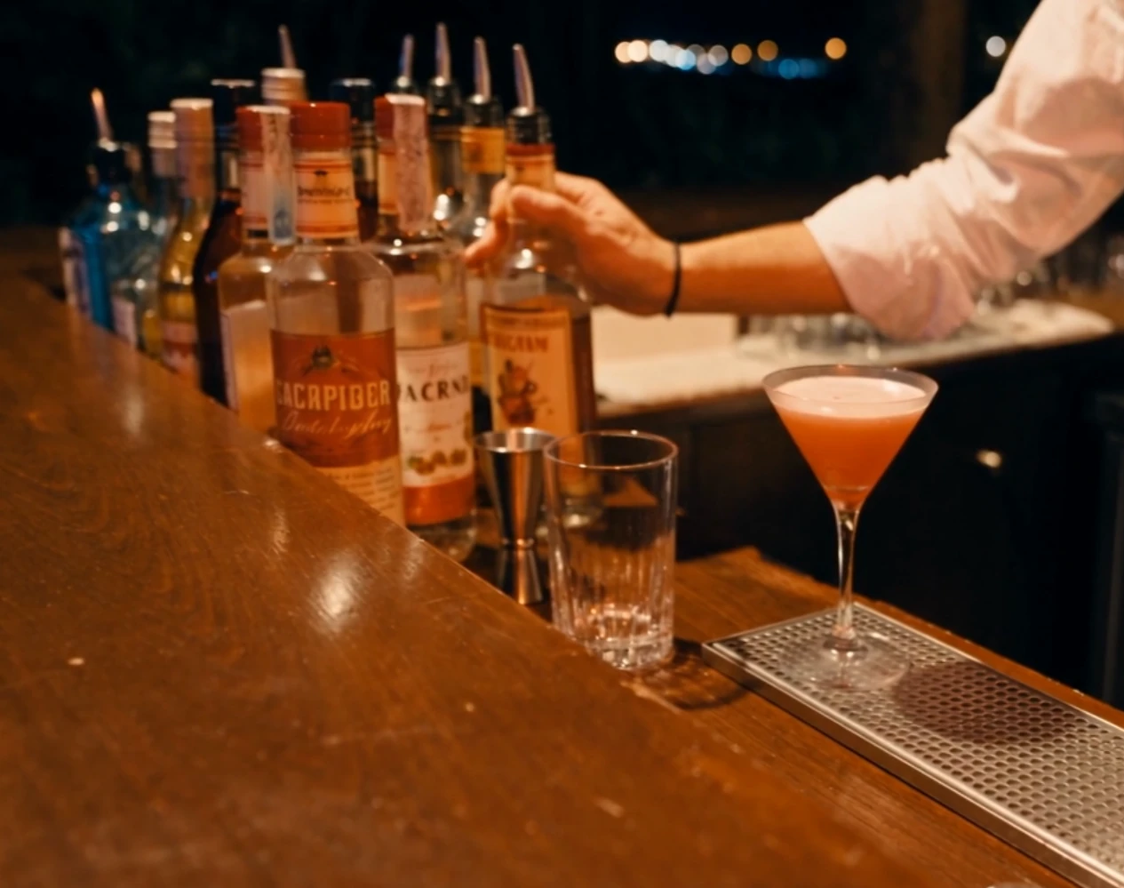 Il banco Switchers di notte: bottiglie con dosatore in linea, jigger e un cocktail servito sul rail